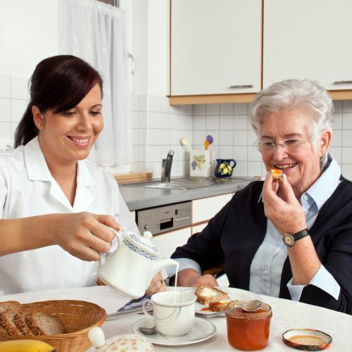 a geriatric nurse helps elderly woman at breakfast